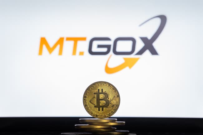 Logo MtGox dietro un bitcoin in piedi su una pila di monete
